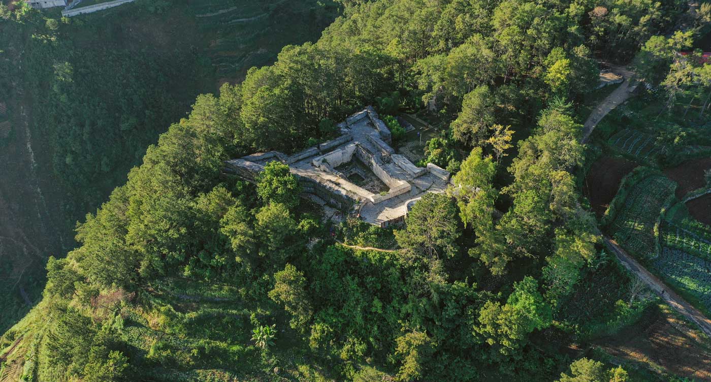 view of an old fortress on a mountain top surrounded by pine trees