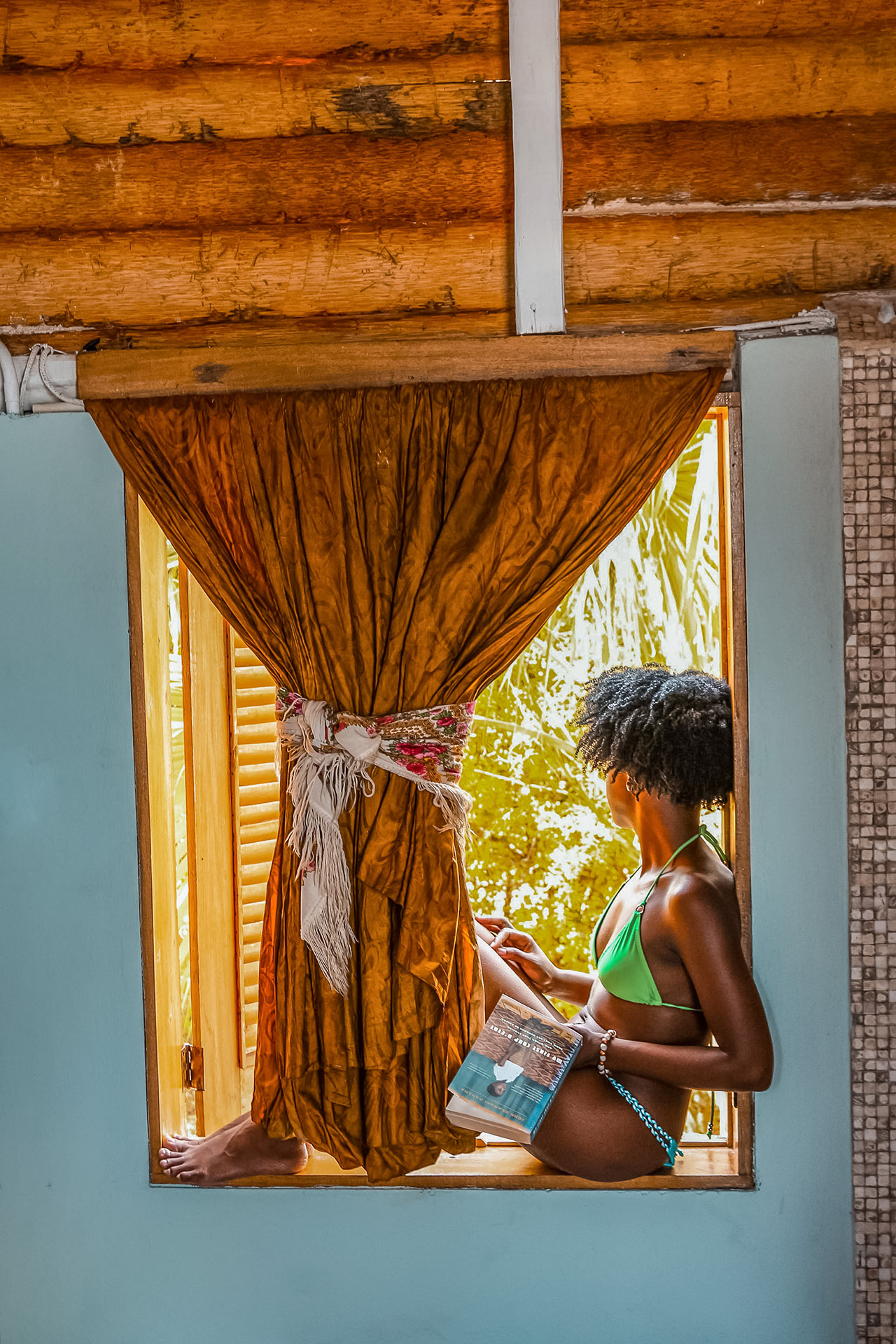 Une femme en bikini se détend dans une fenêtre en tenant un livre