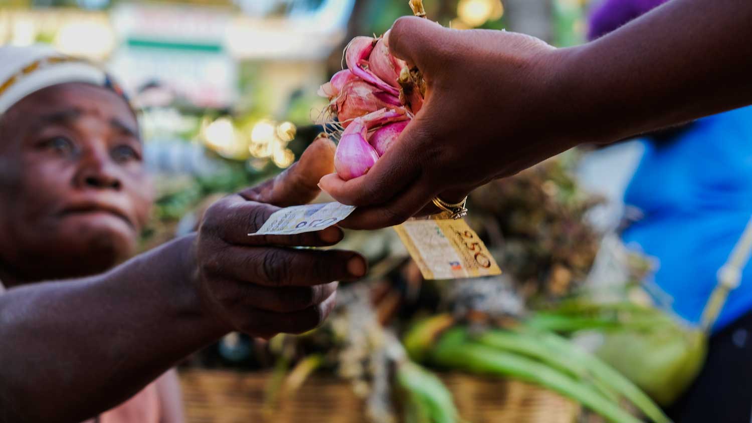 Two women exchanging Haitian gourdes paper money for garlic at a street market