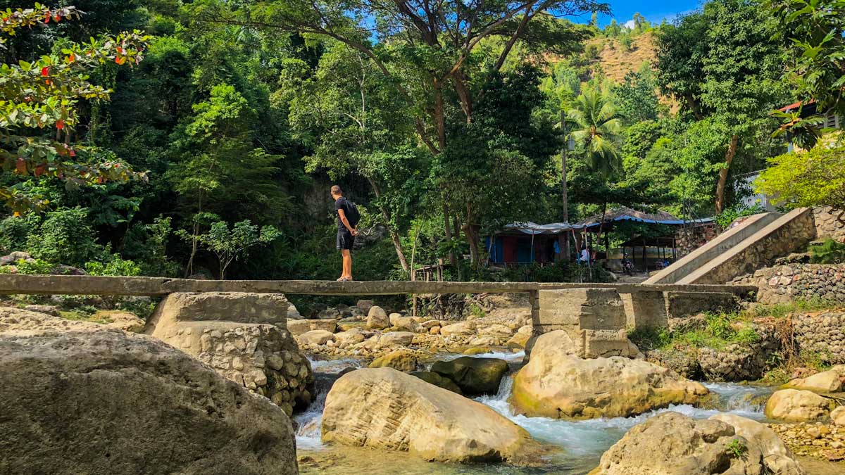 A tourist stands on a stone bridge across rapids at