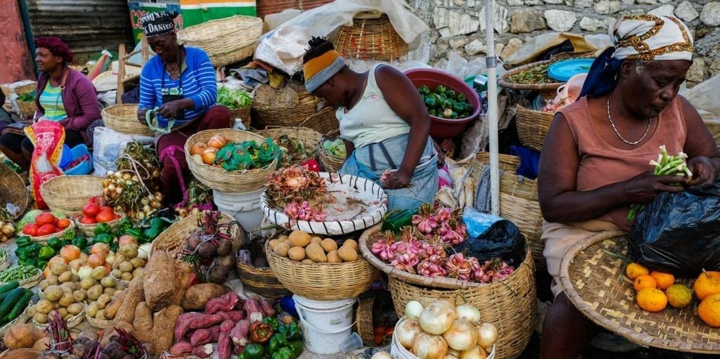 Street vendors surrounded by baskets of colorful fresh produce at a market in Fermathe, Haiti