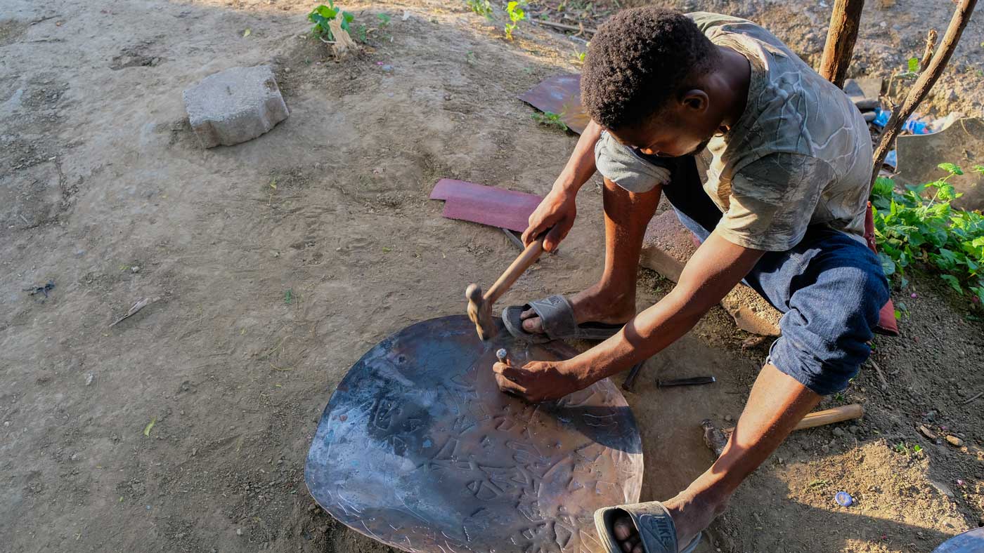 Blacksmith hammers design into metal art in Village Noailles, Haiti