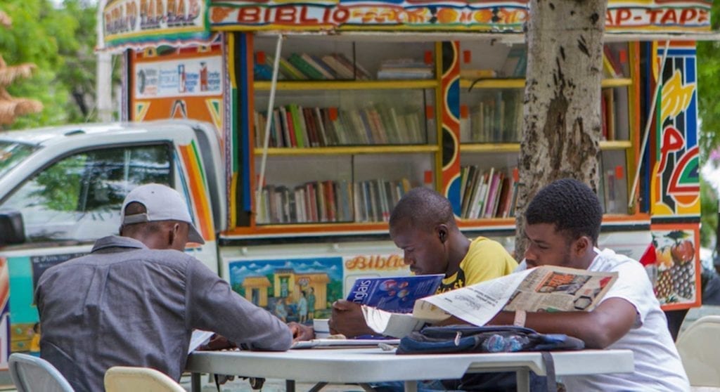 people sitting on chairs reading next to a library bus