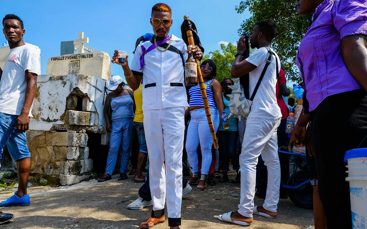 haitian man dressed in white and purple with bottle of rum for fet gede