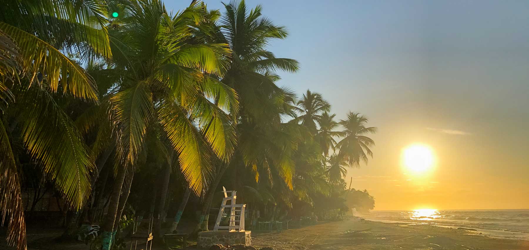 Lever du soleil sur une plage avec des palmiers et un poste de sauveteur