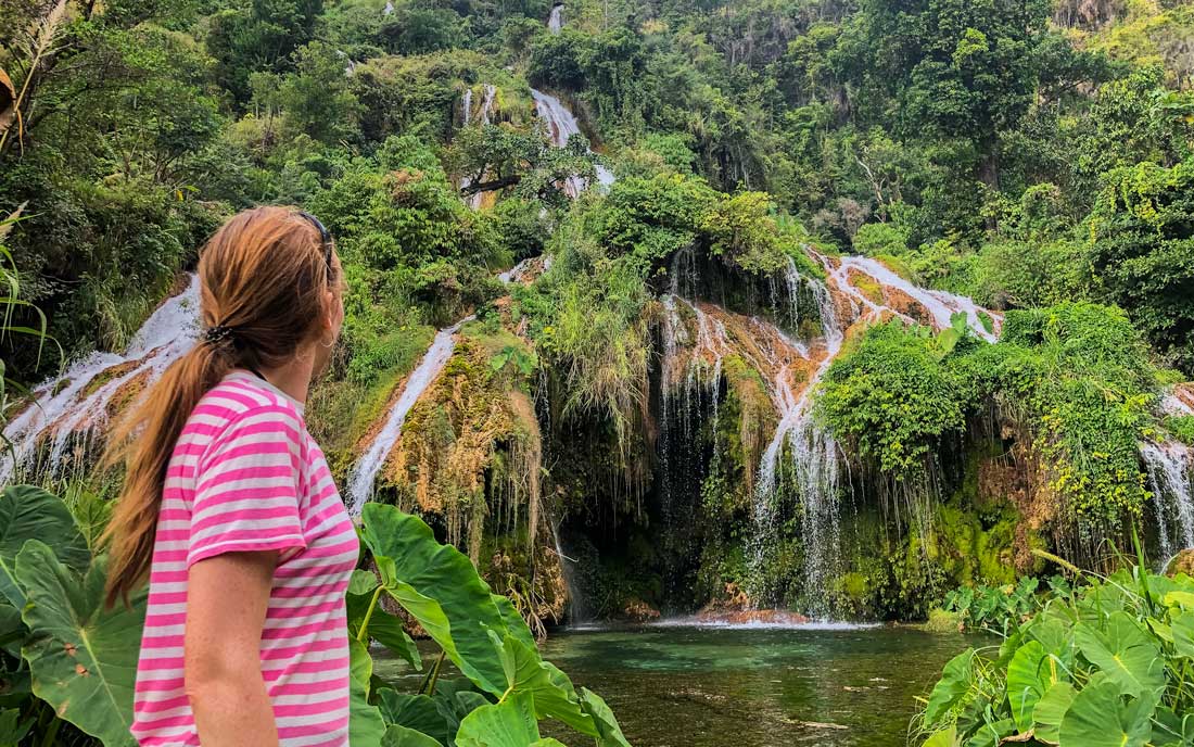 young girl looking at a big waterfall among green plants