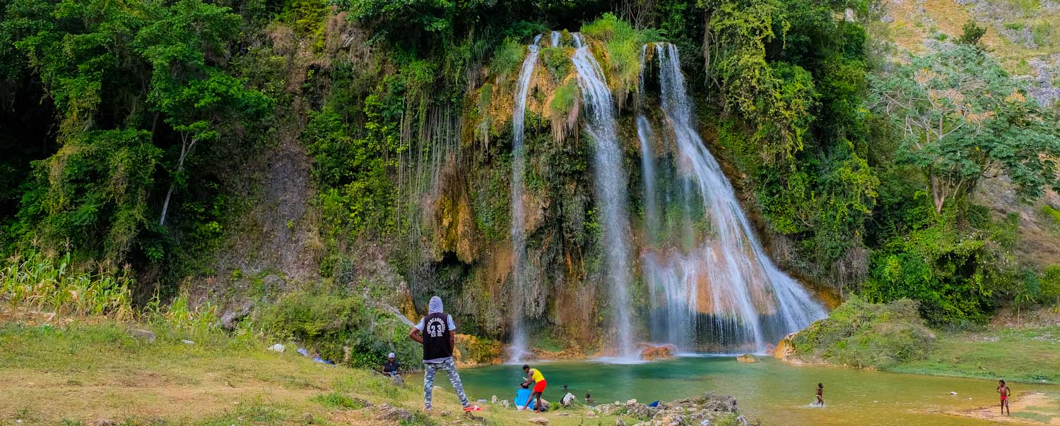 large haitian waterfall splashing into natural pool with people swimming