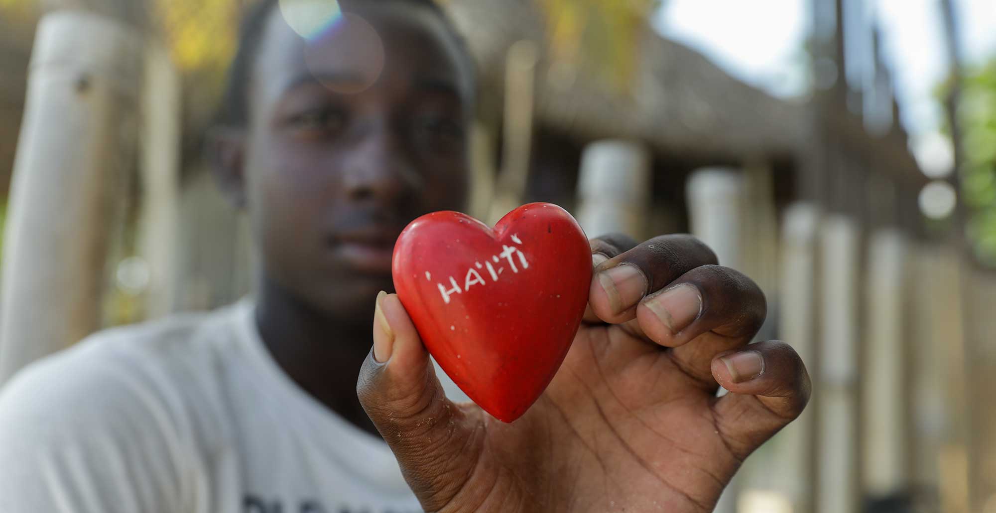 haitian boy holding a red heart carved in limestone, enscribed haïti