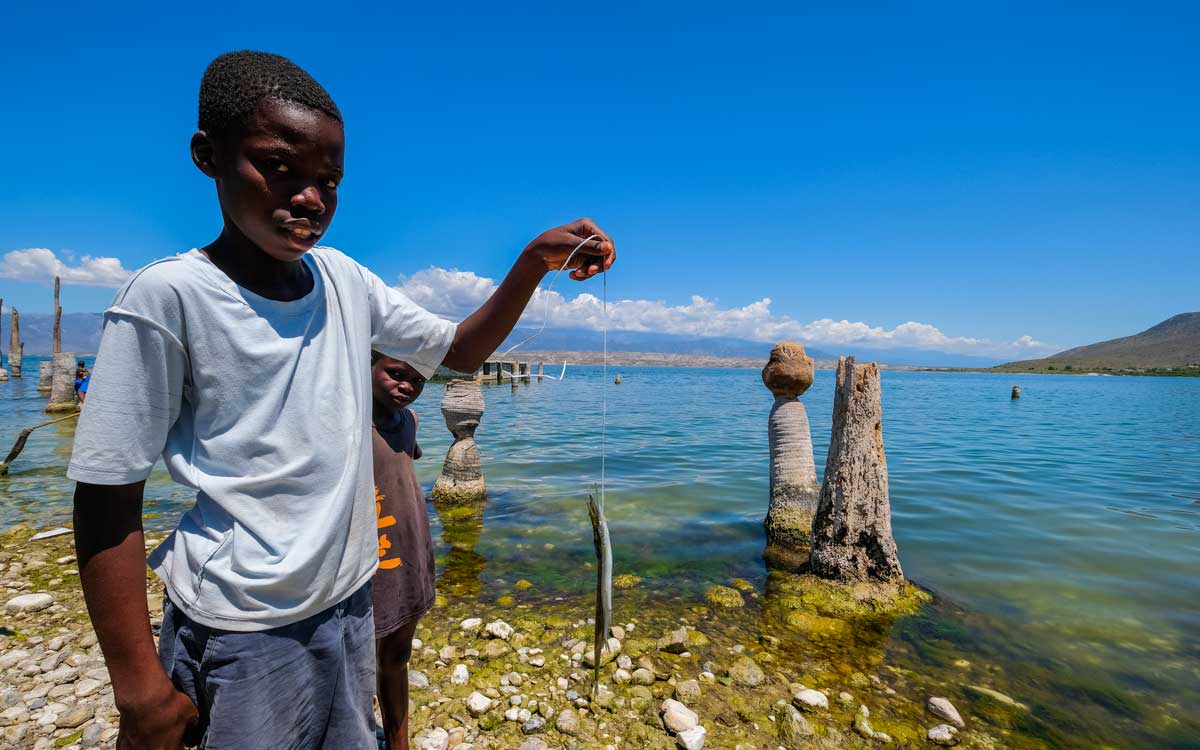 haitian boy with a small fish next to lake