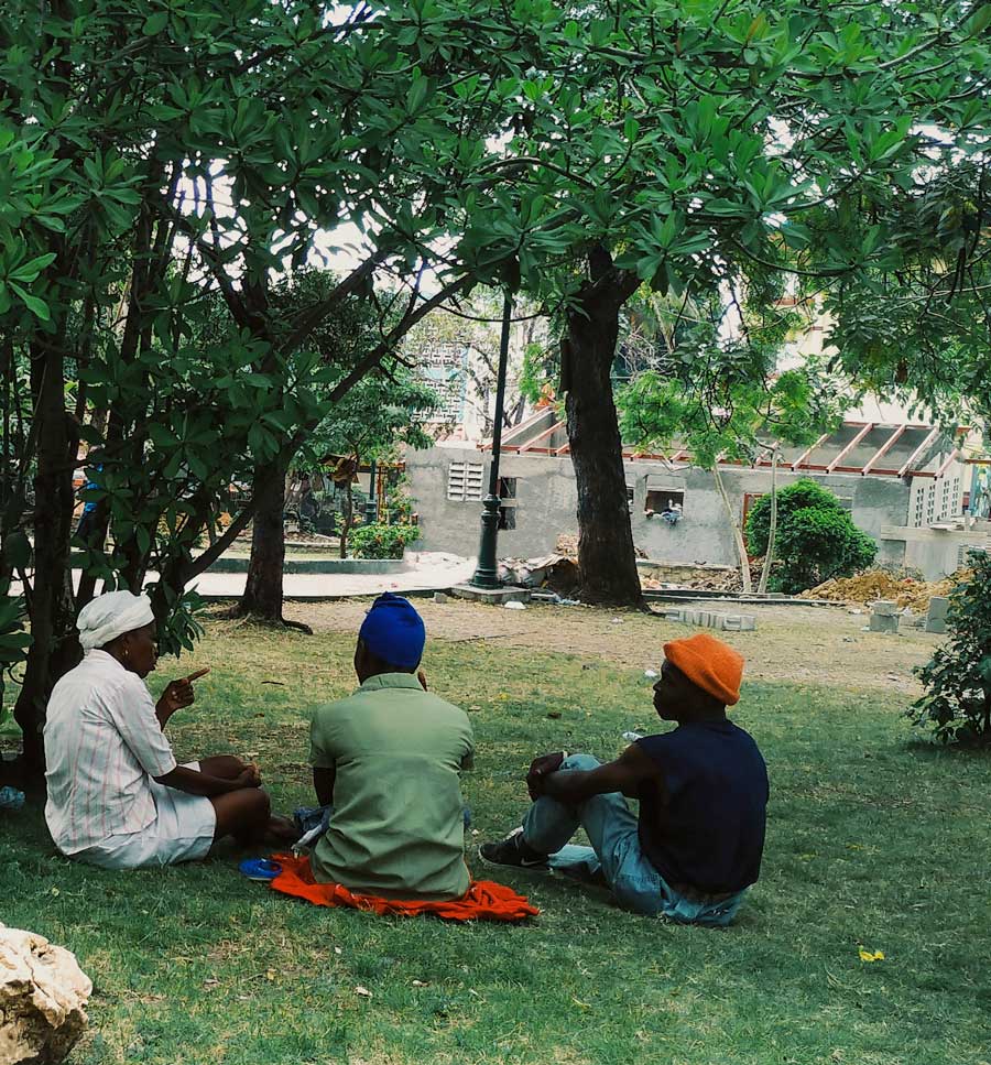 three haitians sitting on grass lawn talking