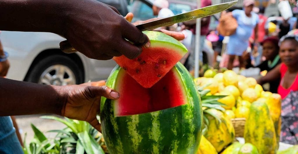 haitian fruit vendor cutting a watermelon