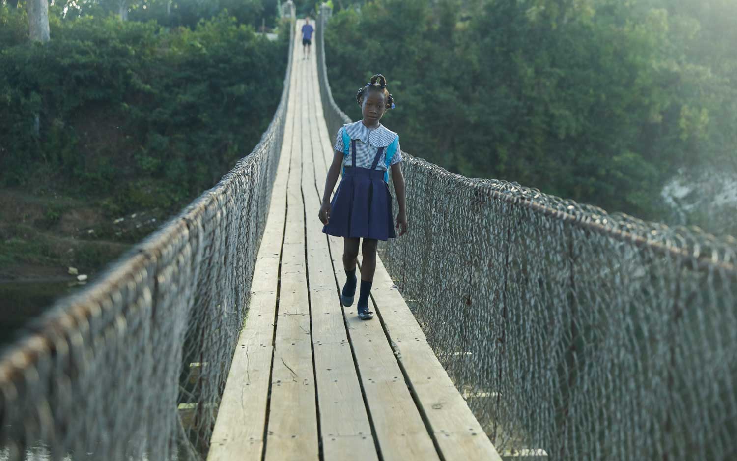 haitian school girl in uniform walking over suspension bridge