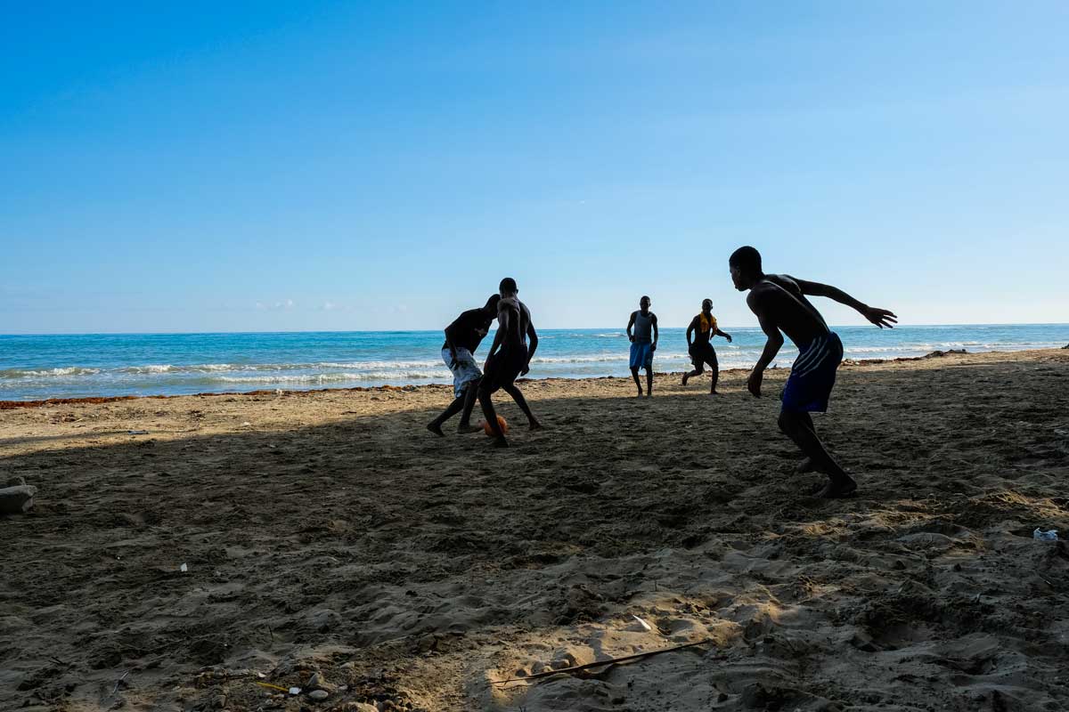 five haitian boys playing soccer on sandy beach