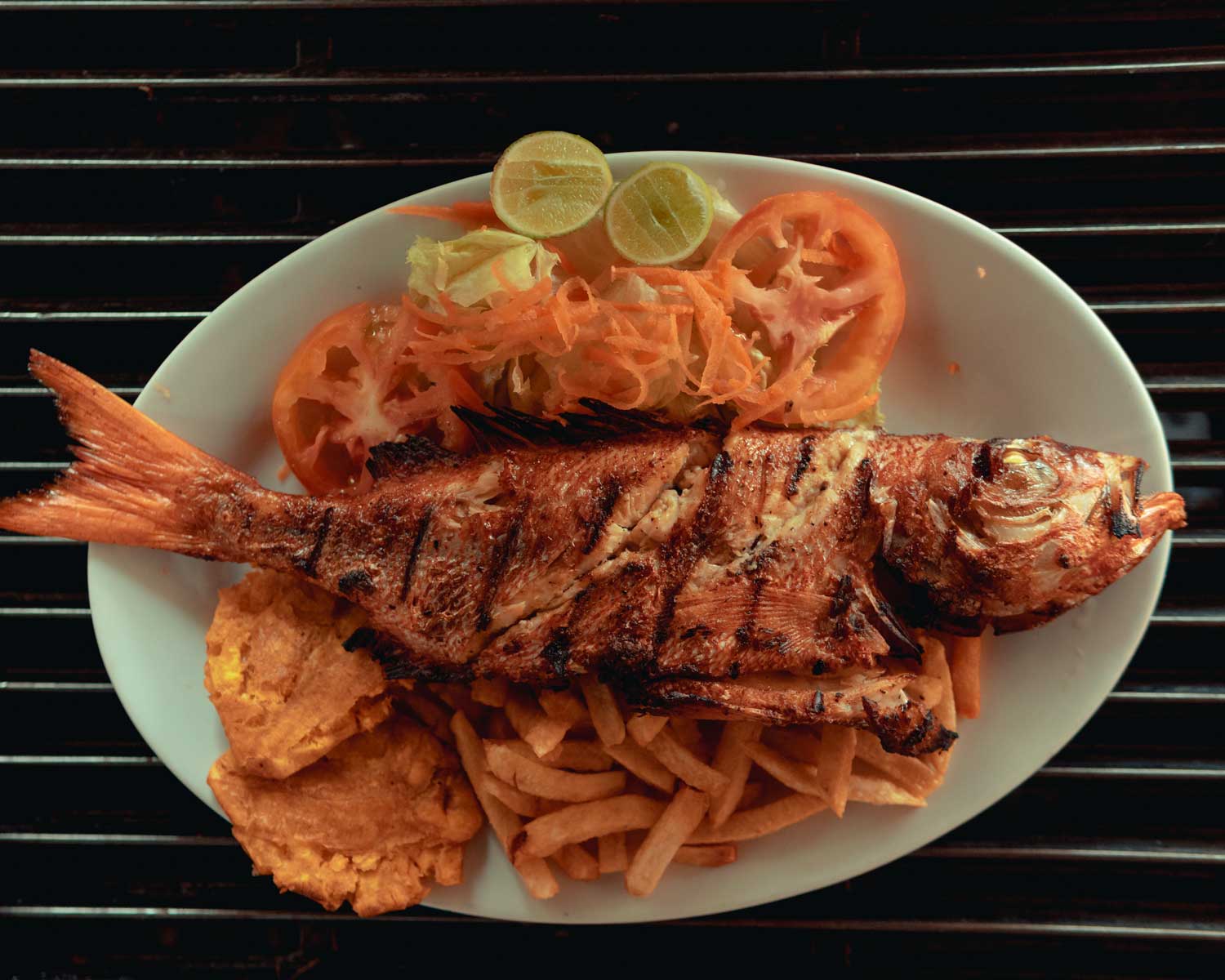 assiette avec poisson grillé, bananes plantains frites, frites et salade