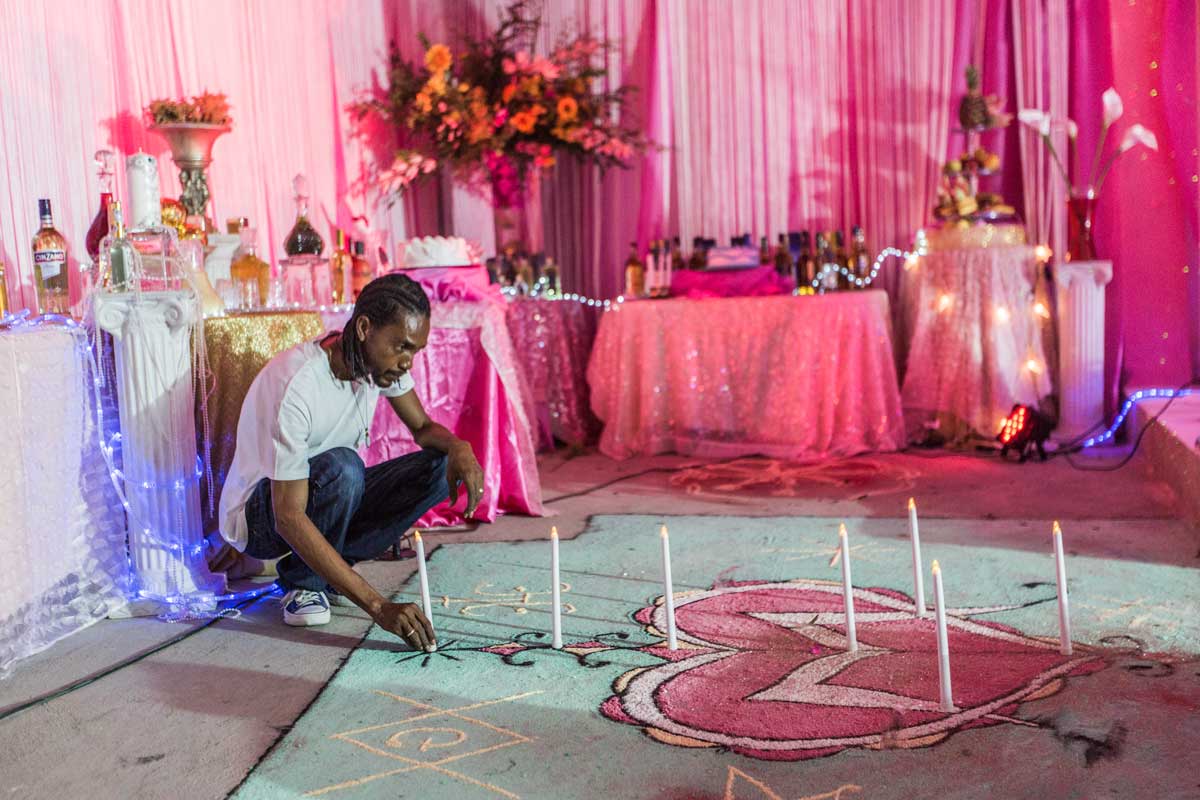 man lighting candles in a lavishly pink decorated room for vodou ceremony